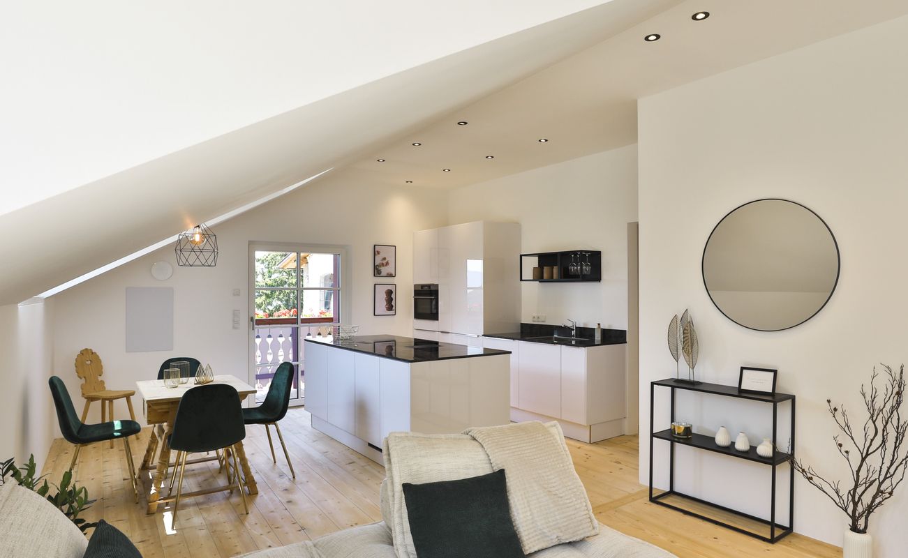 Moderne Küche mit offenem Wohnbereich, helle Wände, Holzfußboden, runde Wandspiegel und Essbereich mit Tisch und Stühlen.